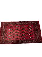 Full view of small rectangular handmade Turkmen rug with red field and repeating geometric guls.