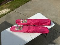 Two red folding chairs packed in carry bags placed on white table outdoors.
