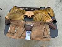 Two used tool belts laid flat on a table showing multiple pockets and compartments