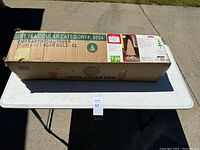 Box of the 6.5 ft rose gold tinsel Christmas tree on a table outdoors, showing product label and details