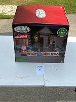 Box of Airblown inflatable Merry Christmas sign showing 12 ft size, image of product set up in front of a home.