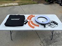 Full lot layout on folding table outdoors showing the ring light, four orange filter covers, and black carrying bag.