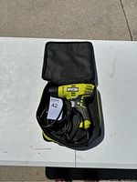 Top view of Ryobi corded drill model D43 inside black soft carrying case on a white table outdoors.