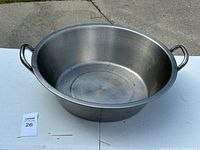 Large round metal pan with two handles placed on a white table outdoors, visible wear inside pan, approximately 22 inches across