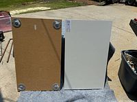 Two IKEA tabletops shown from top and bottom sides, laid out on a blanket outdoors. One tabletop is white laminated on top, brown particleboard underside with metal mounting plates.