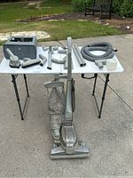 Full view of Kirby vacuum cleaner and multiple accessories displayed on a folding table outside on pavement.