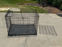 Large black metal wire dog crate placed on outdoor concrete surface with removable black plastic tray beside it.