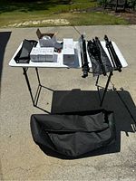 Full view of the white folding table with all items displayed including tripods, boxed bulbs, clamps, light holder, and carrying bags, outdoors on pavement.