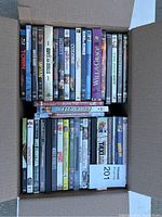 Top-down view of multiple rows of assorted DVDs packed tightly in a box showing a variety of titles and genres.