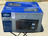 Photo of the Oster microwave oven packaging box showing 1.1 cubic foot capacity and features in Spanish.
