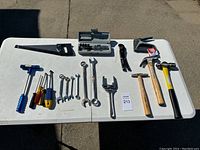Overview of the table showing two handsaws, various screwdrivers, multiple wrenches, and claw hammers arranged in rows.