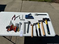 Full view of all tools laid out on a white table, showing the complete lot including hammers, screwdrivers, pliers, staple gun, pry bar and allen wrench.