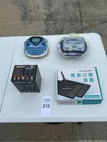 Four office electronics items including two label makers (one in packaging), a boxed electric pencil sharpener, and a boxed USB pen tablet on a white table.