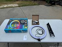 Complete kit on table including boxed ring light, tripod stand, ring light with attached smartphone holder, remote control, and power cable.