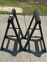 Pair of black Husky saw horses standing on a concrete surface with grassy background, showing side and top views.