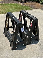Pair of black plastic saw horses placed on concrete outdoors showing the sides and top handle.