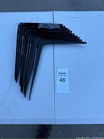 Top view of 10 black metal shelf brackets stacked together on a white surface.