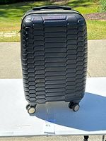 Front view of a black hard shell suitcase with textured honeycomb pattern and four spinner wheels.