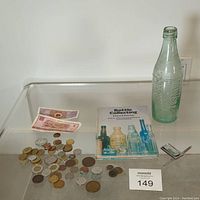 Overview photo showing the bring of foreign coins and notes, the Bottle Collecting book by Edward Fletcher, and the antique Monster bottle with visible lip chips.