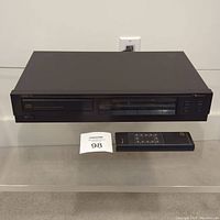Front view of Nakamichi TA-1 CD player with remote control placed beside it, showing the entire unit and remote.