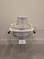 Photo showing stacked Corningware casserole dishes of varying sizes on the Mid-Century teak stand, displaying blue floral patterns and wooden handles.