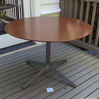 Full view of the round walnut wood veneer dining table top and metal base on outdoor deck.