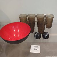 Set showing red interior and black exterior of Krenit bowl, six brown textured glasses, and black and white salt and pepper shakers.