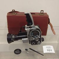 Paillard Bolex P1 8mm Movie Camera with attached Som Berthiot Pan-Cinor lens, lens cap, small metal tools, and leather carrying case in background.