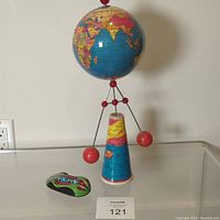 Spinning vintage globe toy on colorful conical stand with two large red weights and Schylling friction toy car beside it