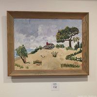 Framed painting showing coastal landscape with large tree, smaller vegetation, sand dunes, and a small cabin near water under cloudy sky.