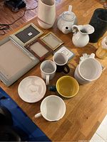 Overview of assorted mugs, frames, pitchers, and vase on a wooden table.