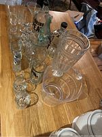 Various assorted glassware on wooden surface including tall glasses, pitchers, decanters, and a glass bowl.