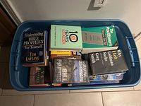 Top view photo showing assortment of books packed in a blue plastic bin. Titles of several books are visible.