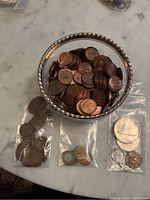 Photo showing assortment of Canadian pennies in silver-rimmed container and three plastic bags with varied coins including a large Jubilee coin
