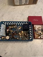 Photo showing a basket with multiple jewelry pieces including several wristwatches, chains, bracelets, and a small jewelry box.