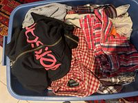 Top view photo of a bin containing assorted men's and women's clothing including hoodies and multiple plaid flannel shirts in various colors.