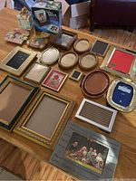 Overview of all 21 assorted picture frames laid out on a wooden table, showing sizes, styles, and materials.