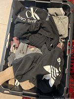 Bin with assorted folded and crumpled clothing items for women and men, visible Calvin Klein and Adidas sweatshirts.