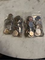 Four clear plastic bags filled with assorted world coins placed on a marble surface.