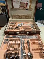 Complete overview of cutlery set organized inside a brown case with peach colored molded trays and beige cloth lining on lid.