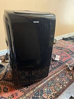 Side angled view of black Danby portable air conditioner on patterned rug, showing unit shape and finish.