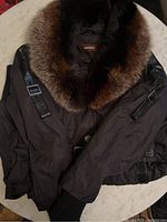 Front view of the folded Danier jacket showing the fur collar and padded black exterior with leather strap details.