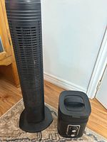 Photo showing the black vertical tower fan and black Westinghouse space heater side by side on a wooden floor and carpet.