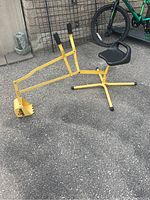 Front side view of the yellow metal children excavator toy with black plastic seat and tripod base.