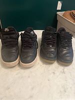 Front view of two pairs of black Nike shoes on marble surface, showing laces and wear on toe areas.