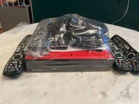 Rogers NextBox with three remote controls on a table, wrapped in clear plastic.