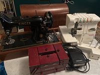 Overview of both Singer sewing machines, red accessory box, foot pedal, and power cord on table