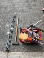 Full view of the basket with a long metal level and sledgehammer placed outside on concrete surface.