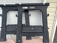 Two black plastic Stanley sawhorses side by side, showing front view with branding and structure.