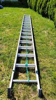 Full view of the aluminum extension ladder laid out on grass showing length and rungs.